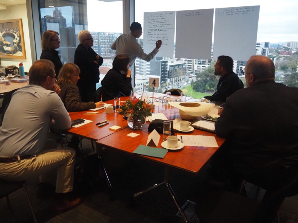 1782736984668 – The Mabo Centre Team in a conference room reviewing notes on large sheets of paper taped to a glass wall, cityscape outside the window.